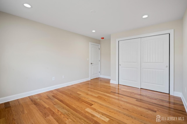 unfurnished bedroom with a closet, recessed lighting, light wood-type flooring, and baseboards