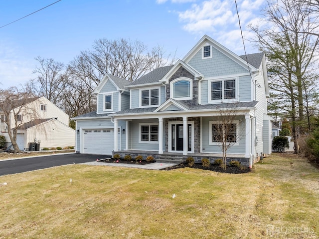 view of front facade with a shingled roof, covered porch, aphalt driveway, and a front yard