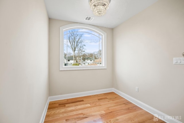 unfurnished room with baseboards, visible vents, a chandelier, and light wood-style floors