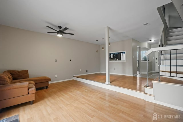 living area with light wood-type flooring, visible vents, a ceiling fan, stairway, and baseboards