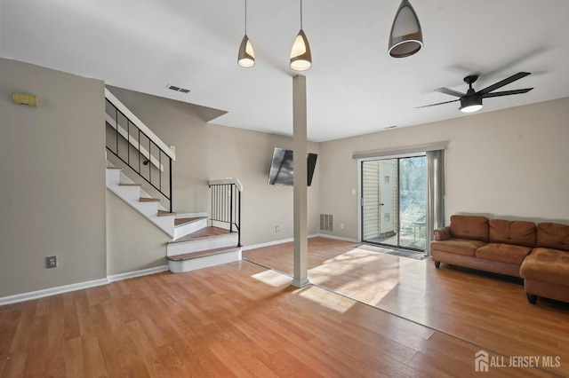 unfurnished living room with wood finished floors, stairs, baseboards, and a ceiling fan