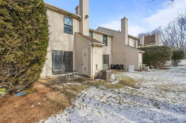 snow covered property featuring a patio area, central AC unit, and a chimney