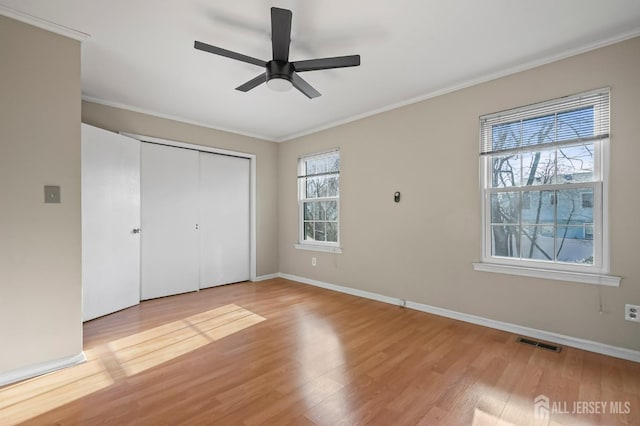 unfurnished bedroom with light wood-style flooring, ornamental molding, a closet, baseboards, and a ceiling fan