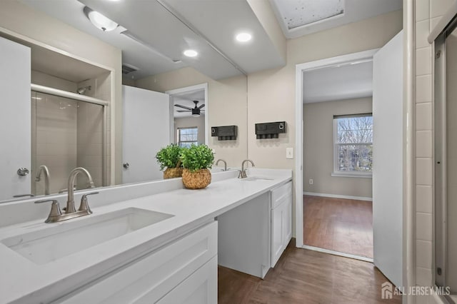 bathroom featuring a ceiling fan, wood finished floors, tiled shower, double vanity, and recessed lighting