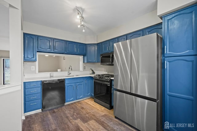 kitchen with stainless steel appliances, a sink, blue cabinetry, dark wood-style flooring, and light countertops