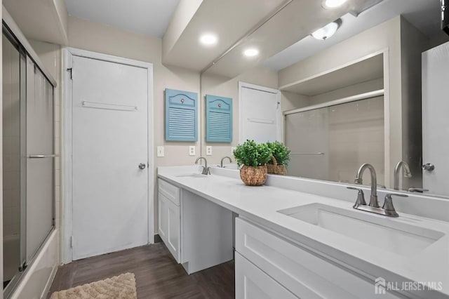 full bathroom featuring wood finished floors, recessed lighting, double vanity, and bath / shower combo with glass door