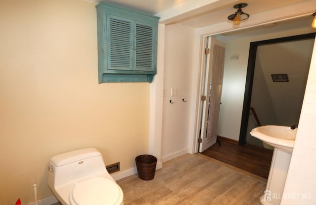 half bath with toilet, a sink, baseboards, and wood finished floors