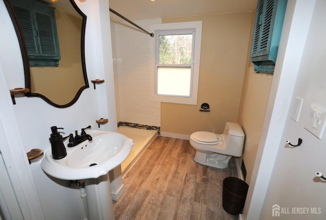 bathroom featuring toilet, baseboards, tiled shower, and wood finished floors