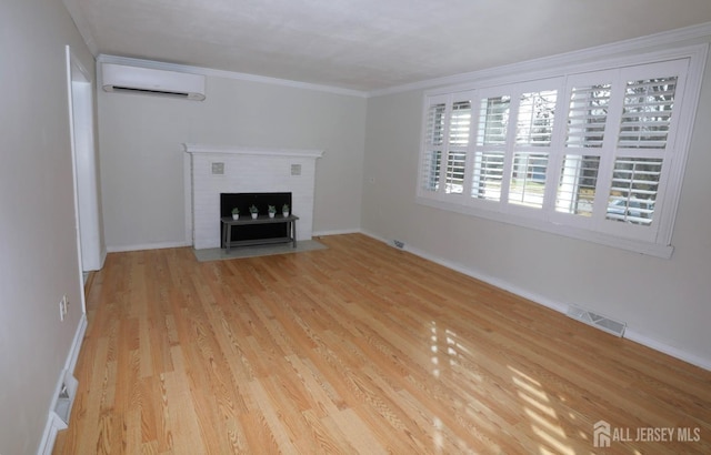 unfurnished living room with a wall unit AC, a fireplace, visible vents, ornamental molding, and wood finished floors