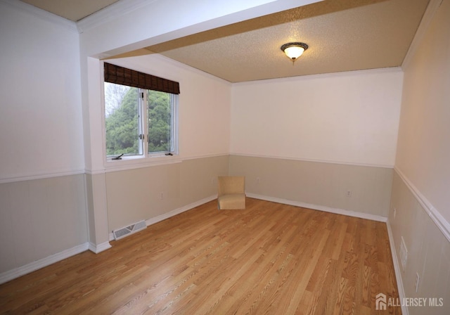 spare room with a textured ceiling, ornamental molding, visible vents, and light wood-style floors