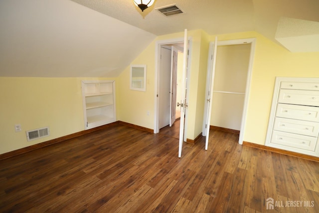 additional living space featuring dark wood-type flooring, visible vents, vaulted ceiling, and baseboards