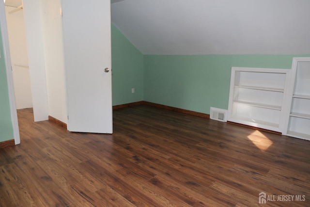 bonus room featuring dark wood-style floors, built in shelves, visible vents, and vaulted ceiling