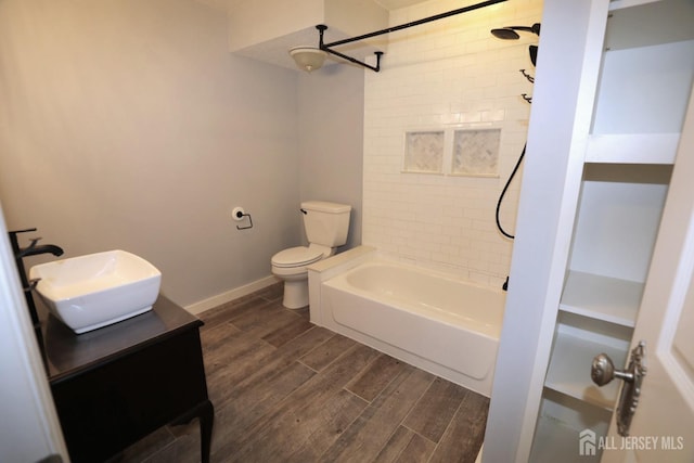 bathroom with wood finish floors, toilet, tub / shower combination, vanity, and baseboards