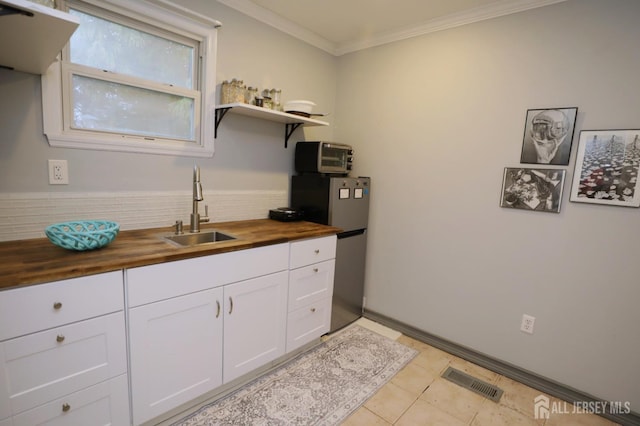 kitchen featuring butcher block countertops, a sink, white cabinetry, ornamental molding, and freestanding refrigerator