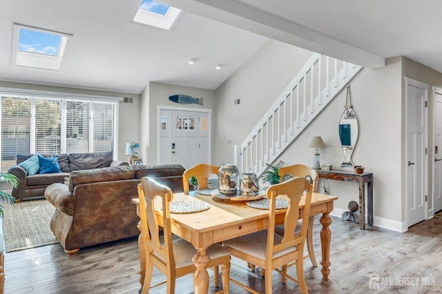 dining area with baseboards, a skylight, stairway, and light wood-type flooring