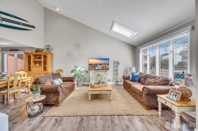living room featuring wood finished floors, baseboards, high vaulted ceiling, and a skylight