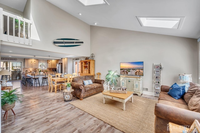 living area featuring light wood finished floors, a skylight, high vaulted ceiling, and visible vents