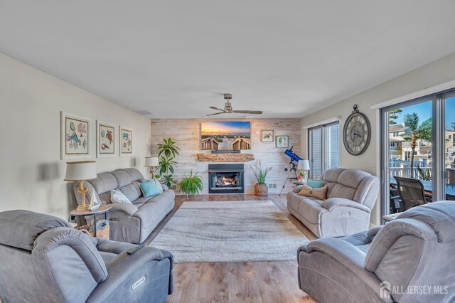 living area with a fireplace with flush hearth, wood finished floors, ceiling fan, and wooden walls
