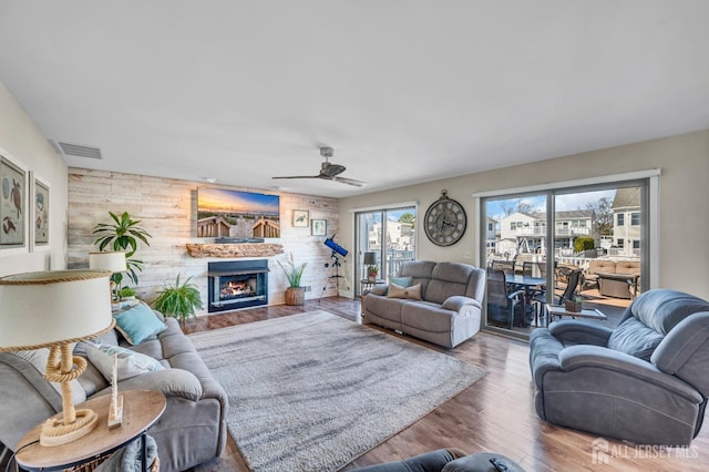 living area with wood finished floors, ceiling fan, visible vents, and a warm lit fireplace