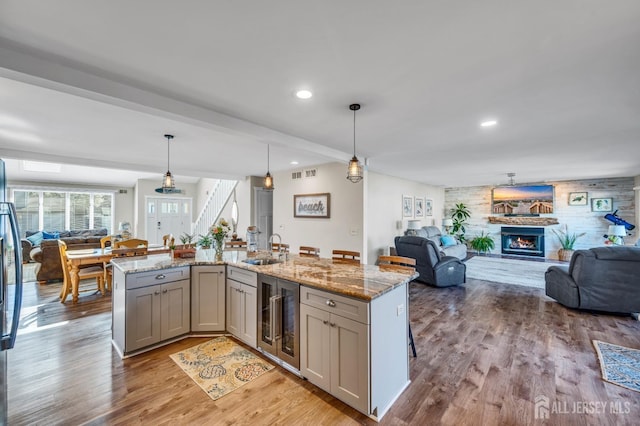 kitchen featuring a sink, beverage cooler, open floor plan, light stone countertops, and wood finished floors
