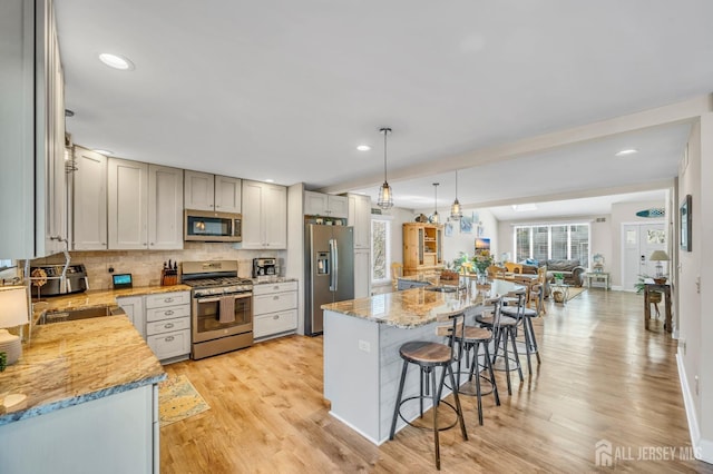 kitchen featuring recessed lighting, decorative backsplash, a breakfast bar, light wood-style flooring, and appliances with stainless steel finishes