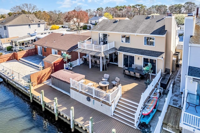rear view of property with a fenced backyard, a deck with water view, outdoor dining area, a residential view, and roof with shingles