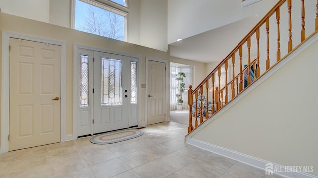 entryway with stairway, a high ceiling, tile patterned floors, and baseboards