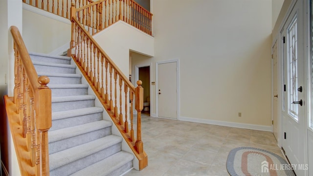 foyer entrance with stairs, baseboards, and a high ceiling