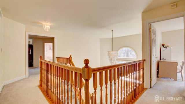 hallway with light carpet, an upstairs landing, baseboards, and a chandelier