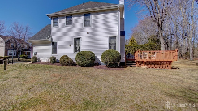 back of property with a deck, a lawn, a chimney, and a shingled roof