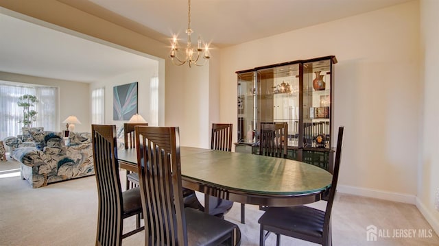 dining room featuring light carpet, a chandelier, and baseboards