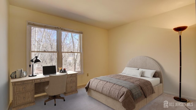 bedroom featuring light carpet, an office area, and baseboards