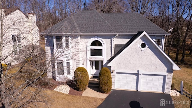 view of front of property featuring asphalt driveway, stucco siding, a garage, and a shingled roof