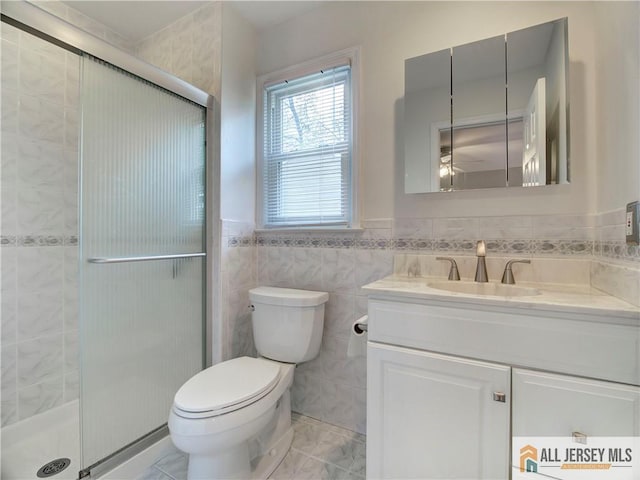 bathroom with tile walls, a shower stall, vanity, toilet, and a ceiling fan