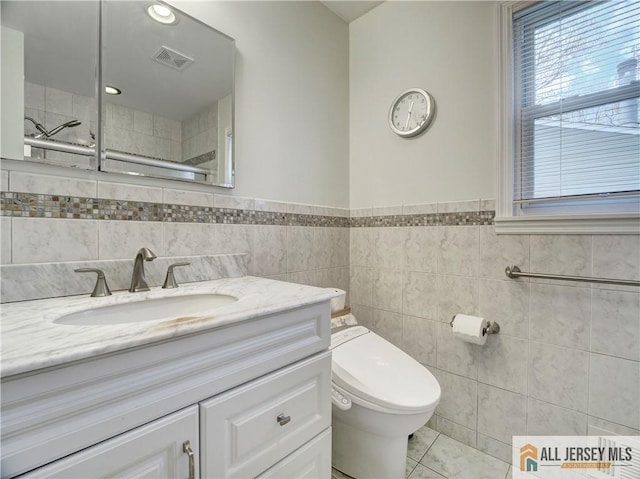 full bathroom featuring tile walls, toilet, vanity, tile patterned flooring, and a wainscoted wall