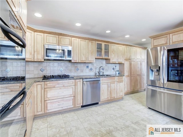 kitchen featuring appliances with stainless steel finishes, light brown cabinets, a sink, stone counters, and tasteful backsplash