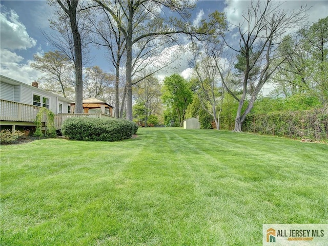 view of grassy yard featuring a wooden deck, a shed, and an outbuilding
