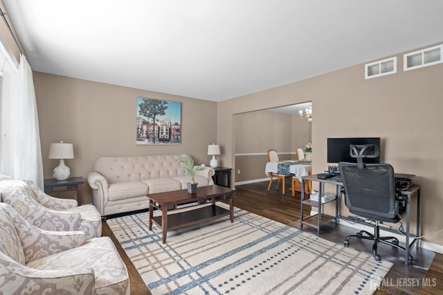 living room featuring a notable chandelier, baseboards, visible vents, and wood finished floors
