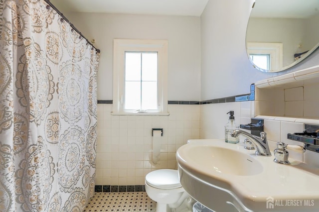 full bathroom featuring tile walls, toilet, a wainscoted wall, a shower with shower curtain, and a sink