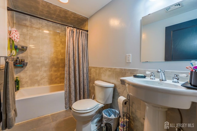 bathroom with toilet, tile patterned floors, shower / bath combo with shower curtain, tile walls, and a sink