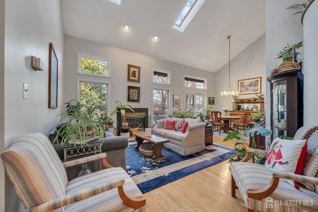 living room with high vaulted ceiling, a skylight, hardwood / wood-style flooring, and a notable chandelier