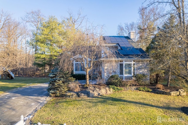 view of front facade with solar panels, a chimney, and a front yard