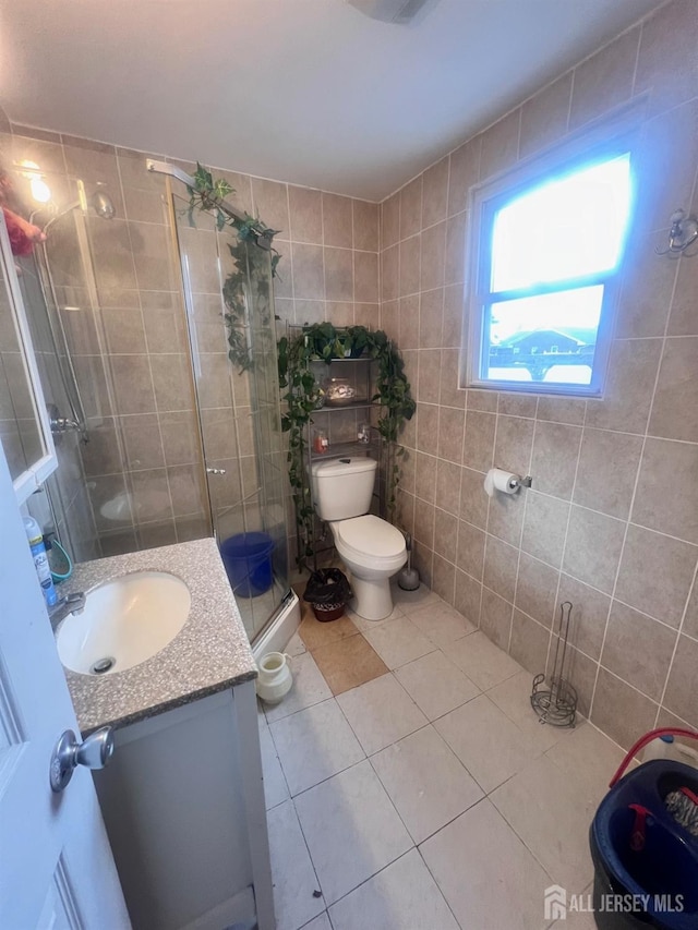 bathroom with vanity, a shower with door, tile patterned floors, toilet, and tile walls