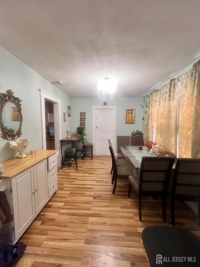 dining space with a notable chandelier, a textured ceiling, and light wood-type flooring