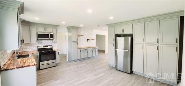 kitchen with tasteful backsplash, butcher block counters, stainless steel appliances, light wood-type flooring, and sink