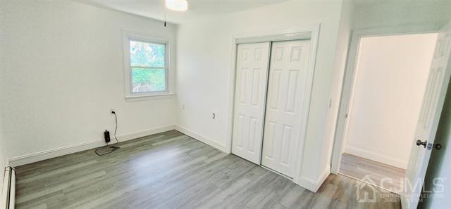 unfurnished bedroom featuring light hardwood / wood-style flooring, a closet, and a baseboard radiator