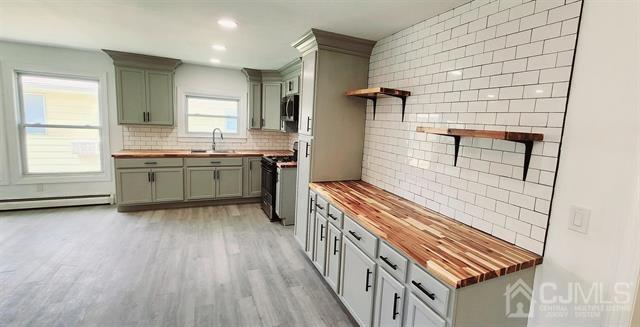 kitchen with light wood-type flooring, butcher block counters, tasteful backsplash, and range