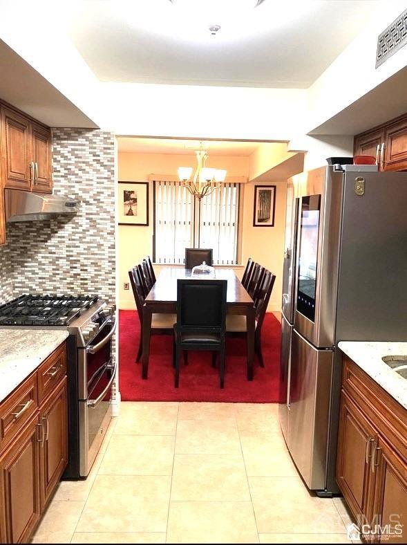 kitchen featuring an inviting chandelier, appliances with stainless steel finishes, backsplash, and light tile patterned floors