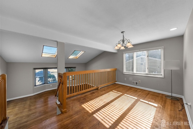 interior space featuring visible vents, vaulted ceiling with skylight, baseboards, and wood finished floors