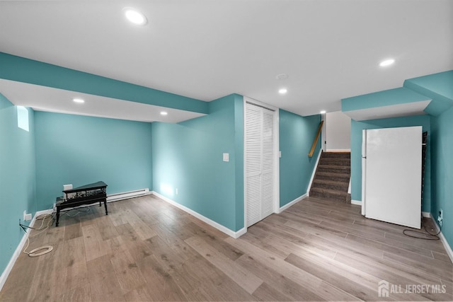 finished below grade area featuring wood finished floors, recessed lighting, freestanding refrigerator, stairs, and a baseboard heating unit